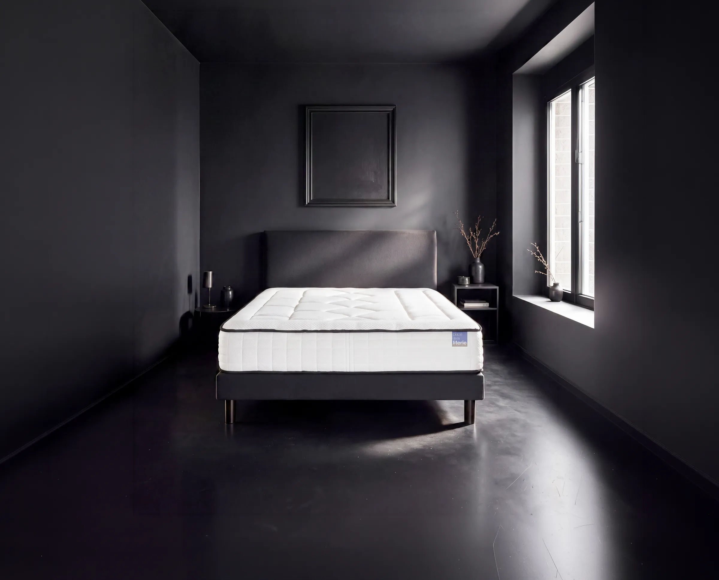 Matelas blanc sur sommier noir dans une chambre aux murs sombres